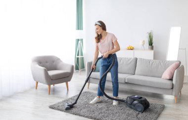 Neşeli kadın temizlikçi, elektrikli süpürgeyle evi temizliyor, uzun bir portre. Pozitif genç kadın ev işleri yapıyor, evini temiz tutuyor. Ev hijyeni kavramı