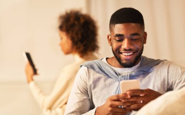 Hile yapıyor. Siyah adam telefonda konuşuyor, kanepede kız arkadaşının yanında oturuyor.