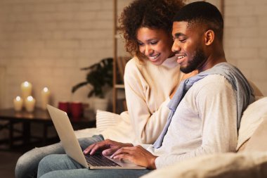 Heyecanlı afro çift dizüstü bilgisayarda sörf yapıyor. Evdeki sıcak kış atmosferinin tadını çıkarıyor.