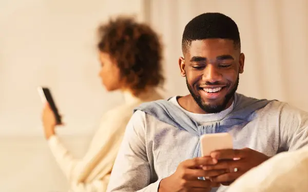 stock image Cheating. Black man chatting on phone, sitting next to girlfriend on couch