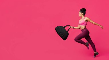 Sağlıklı yaşam tarzı kavramı. Çekici, spor düşkünü, zinde bir zenci kadın kırmızı stüdyo arka planında spor salonuna koşmak için yalvarıyor.
