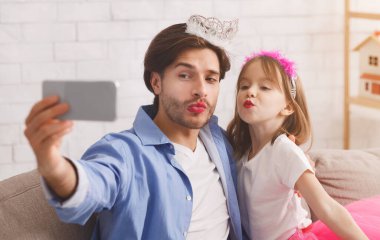 Babası ve güzel kızı evde selfie çekiyor, taç takıyor ve ruj sürüyor, ördek suratları yapıyor.