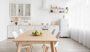 Mutfak ve yemek odasının çağdaş minimalist iç mekanı. Çatal bıçaklı beyaz mobilyalar ve İskandinav tarzı sandalyeli yemek masası. Modern ışık tasarımı