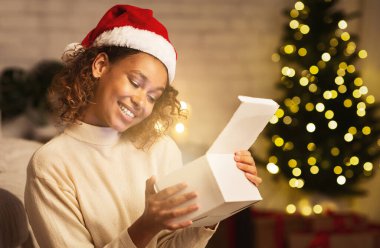 Noel büyüsü. Heyecanlı siyah kız evde Noel ağacının önünde hediye kutusunu açıyor.