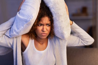 Sinirli kadın yastıkla kulaklarını kapatıyor, gürültücü komşulardan muzdarip.