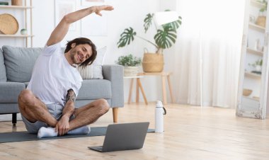Aktif, genç ve neşeli bir adam sabah jimnastik yapıyor, yoga minderinde oturuyor ve geriniyor, fotokopi çekiyor.
