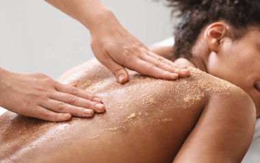 Afrika kökenli, rahat bir bayan kaplıca salonunda cilt fırçalama işlemi yaptırıyor, yakın plan. Spa terapisti, lüks kaplıcalarda uyuyan siyah kadına vücut maskesi takıyor.