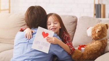 Küçük tatlı bir anaokulu kızı babasını Babalar Günü 'nde karşılıyor, elinde hediye kartıyla babasına sarılıyor, bedava uzay boşluğu.