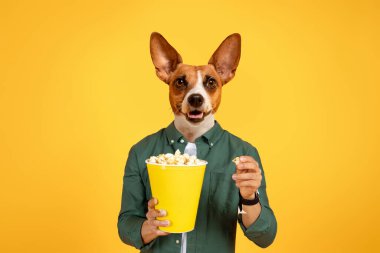 İnsan kafalı bir köpek gülümsüyor ve elinde sarı bir kova patlamış mısır tutuyor. O, yeşil düğmeli bir gömlek giyiyor ve diğer elinde bir parça patlamış mısır tutuyor. Arka plan sarı..