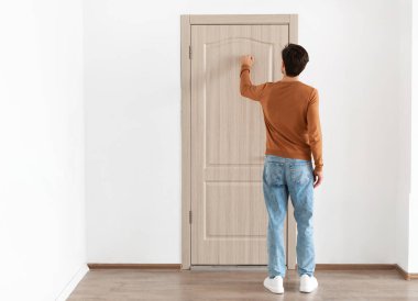 Arkaya bakan genç adam ahşap kapıyı çalıyor, erkek ziyaretçi ön kapıda duruyor, misafir içeri girmek istiyor, bedava fotokopi alanı, tüm vücut uzunluğu.