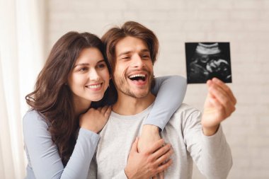 Bebeklerinin ultrason taramasına bakıp evde sarılıp kaynaşan mutlu genç çift.