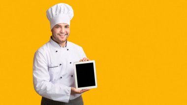 Professional Cook Guy Showing Empty Tablet Screen Standing In Studio Over Yellow Background. Panorama, Mockup