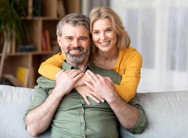 Güzel, gülümseyen orta yaşlı bir çiftin portresi. Evde kucaklaşan neşeli, olgun eşler. Oturma odasında birlikte poz verirken.