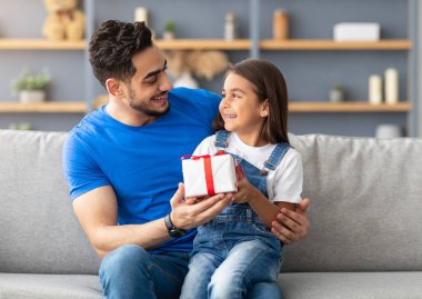 Bu hediye senin için. Sevgi dolu bir kızın portresi babasının kucağında oturuyor ve onu baba günü ya da doğum günüyle karşılıyor, paketlenmiş bir hediye kutusu tutuyor, mutlu bir aile tatilini evde kutluyor.