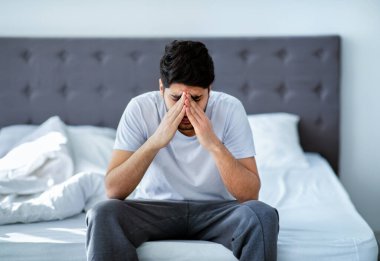 Erkek depresyonu. Mutsuz Arap adam yatakta oturup sorunları düşünüyor, ellerle yüzünü kapatıyor, kopyalama alanı yaratıyor. Stres, ilgisizlik ve zihinsel sağlık sorunu kavramı.