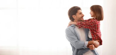 Yakışıklı baba tatlı kızını kucağında tutuyor, birbirine bakıyor. Pencere arkası, fotokopi alanı olan panorama.