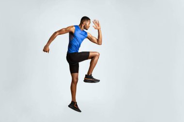 Egzersiz yapıyorum. Yüksek dizli, bacak kaldıran ve el sallayan kollu kaslı afro adamın tam boy portresi.