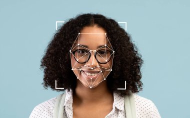 Kıvırcık saçlı ve gözlüklü genç bir Afrikalı Amerikalı kadın kameraya gülümsüyor, rahatlatıcı mavi bir arka planda yüz tanıma programı sergiliyor..