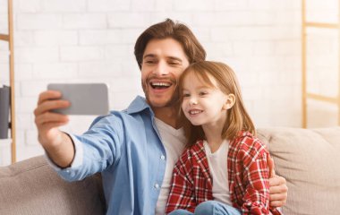 Birlikte mutlu anlar. Duygusal genç adam güzel kızıyla evde selfie çekiyor, akıllı telefon kullanıyor, boş alan kullanıyor.