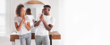 Genç bir Afrikalı Amerikalı çift şık, parlak bir odada duruyor, gülümsüyor ve birbirlerini eğlendiriyorlar, asgari dekor ve doğal ışıkla çevrili..