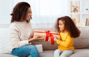 Anneler Günü. Küçük kız, mutlu anneye hediye veriyor. Evdeki koltukta oturuyor..