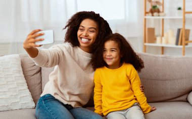 Mutlu Afrika kökenli Amerikalı anne ve kızı akıllı telefon kullanarak evde otururken selfie çekiyor. Seçici Odaklanma