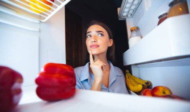Düşünceli ev hanımı mutfaktaki buzdolabına bakıyor, içeriden bakıyor.