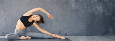 Genç bir kadın, minimalist kapalı bir alanda yoga yaparken yan esneme hareketleri yapıyor.