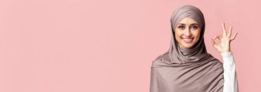 Her şey yolunda. Mutlu İslamcı kadın stüdyoda pembe arka plan üzerinde jest yapıyor.