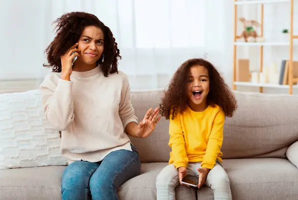 stock image Loud Child. Little Daughter Shouting While Afro Mother Talking On Phone Sitting On Couch At Home