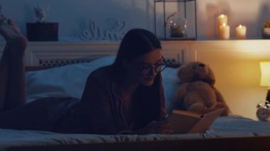 Gece iç çamaşırlı bir kadın uyumadan önce kitap okuyor, akşamları yatakta yatıyor.