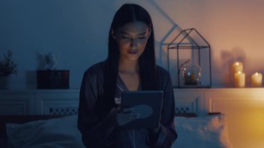 Neşeli kız dijital tablette geziniyor, uyumadan önce yatakta dinleniyor.