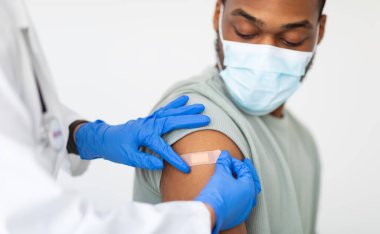Siyah Adam Covid-19 'a karşı aşı oluyor, Doktor Coronavirus' a antiviral aşı enjekte ettikten sonra beyaz arka planda Coronavirus 'a karşı alçı uyguluyor. Kırpılmış, Seçici Odaklanma