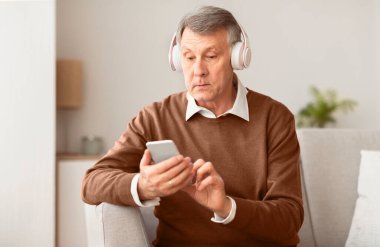 Müzik uygulaması. Kablosuz kulaklıklı son sınıf öğrencisi akıllı telefon kullanarak koltukta oturan şarkıları dinliyor. Seçici Odaklanma