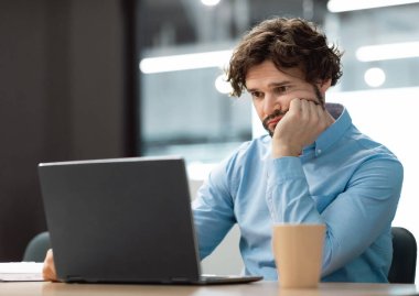 Portrait of sad bored business man sitting at desk using pc, leaning head on hand looking at screen. Upset stressed guy suffering job problems, reading bad negative news at office, free copy space clipart