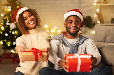 Noel hediyeleri. Noel Baba şapkalı siyah bir çift ellerinde hediyeler ve Noel ağacının önünde gülümsüyor.