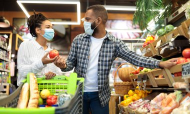 Market alışverişi. Maskeli Afrikalı bir çift birlikte sebze alıyor. Süpermarkette alışveriş arabasıyla ayakta duruyorlar. Alıcılar Sağlıklı Yemek Konseptini Seçiyor