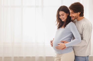 Gelecekteki ebeveynler. Mutlu bir çiftin evde pencerenin önünde beklerken kucaklaşmasını ve gülümsemesini bekliyorum.