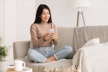 Hafta sonu evde. Kız akıllı telefondan sosyal ağları kontrol ediyor, kanepede dinleniyor.