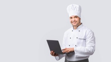 Şef Adam dizüstü bilgisayarını kullanarak Beyaz Stüdyo Arkaplanındaki Yeni Tarifleri Tarıyor. Mutfak web sitesi. Panorama