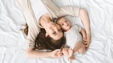 Anneliğin mutluluğu. Gülümseyen anne ve onun tatlı küçük bebeği yatağında uzanmış, üst tarafta.