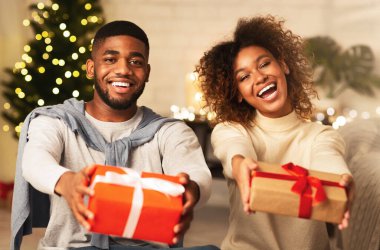 Noel hediyesi kutuları tutan ve Noel ağacının önünde gülümseyen siyah bir çift.