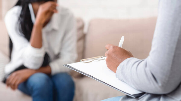 Unrecognizable female psychologist noting problems of woman patient at therapy session,selective focus