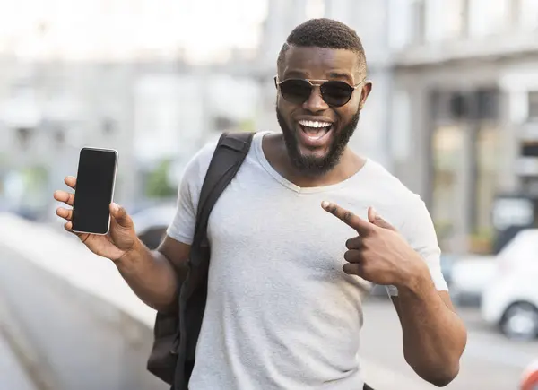 stock image Hey something new. Happy african guy pointing his cellphone with black blank screen for advertisement outdoor, panorama