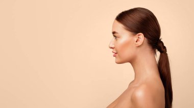 Stüdyodaki gri arka planda boş alan pozuna bakan gömleksiz genç bir kadının yan görünümü. Reklam afişi için kadın portresi. Panorama