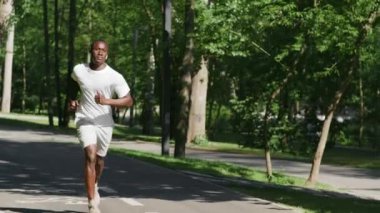 Sabah koşusu egzersizi. Afrikalı Amerikalı bir adamın şehir parkında ağır çekimde koşarken çekilen görüntüsü.