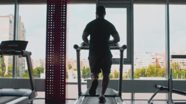 Tecrit spor eğitiminden sonra. Beden eğitiminde koşu bandında koşan, şehir manzarasına bakan bir adamın arkası.