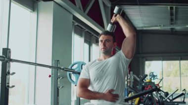 Spor salonunda dambılla spor yapan profesyonel bir sporcu, triseps kaslarını çalıştırıyor, ağır çekimde çalışıyor.