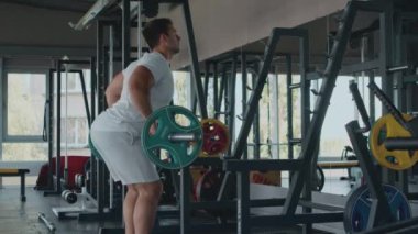 Sporcu halterle egzersiz yapıyor, kaslarını esnetiyor, antrenman yapıyor ve spor salonuna geri dönüyor.