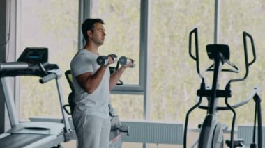 Spor salonunda dambıllarla çalışan genç bir adam, pazı egzersizi konsepti.